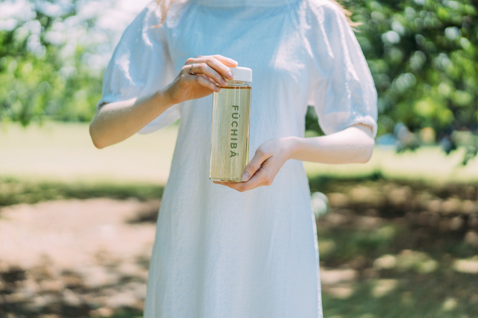屋外でFŪCHIBĀのボトルを両手に持つ女性