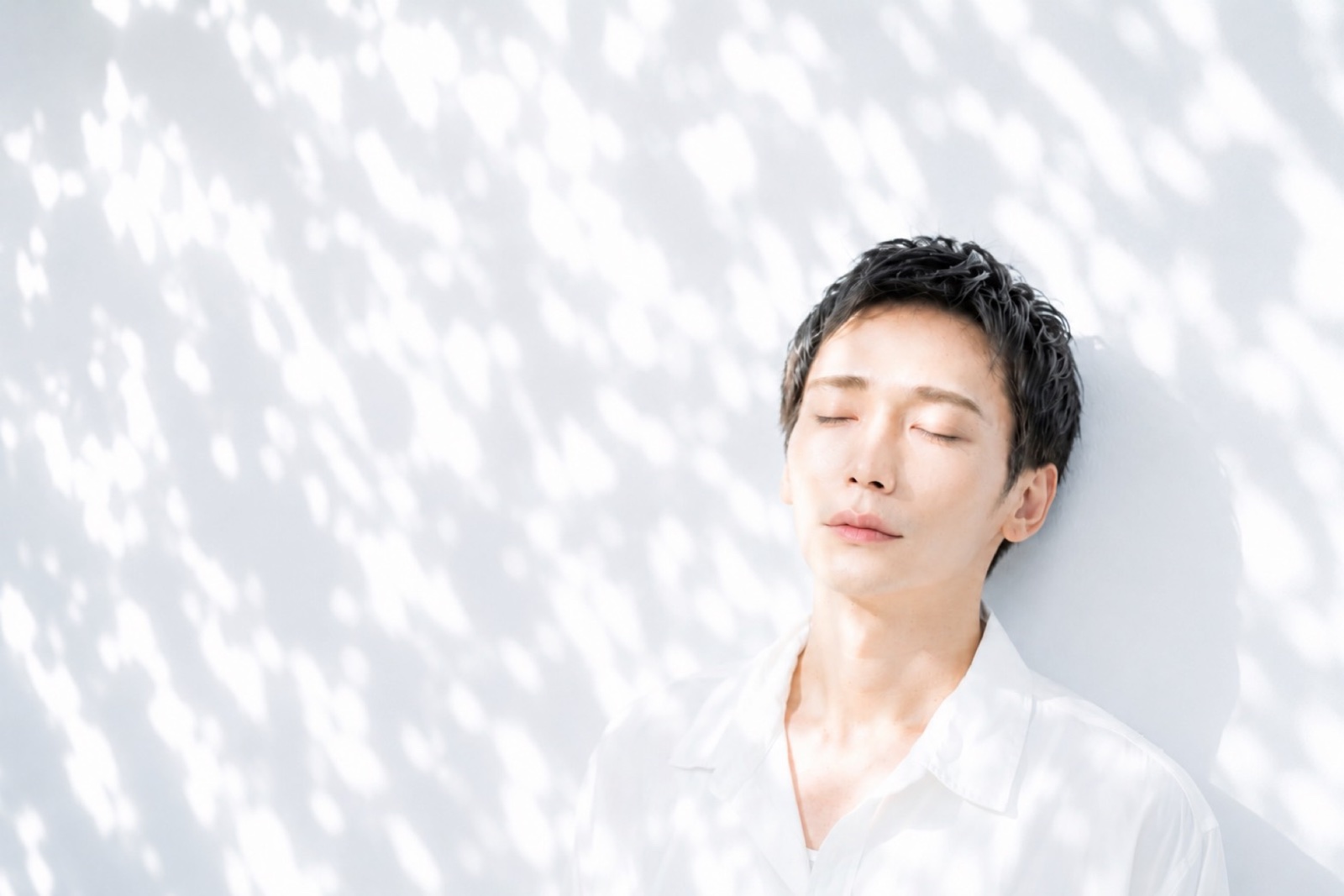 木漏れ日の中で目を閉じ、静かに光を浴びる男性